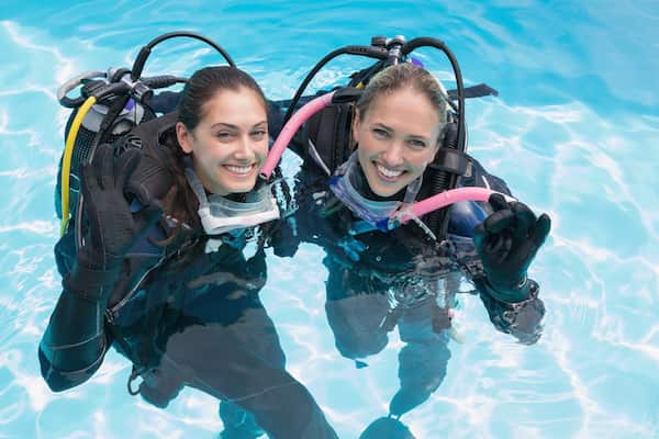 Two women scuba diving in the water wearing wetsuits.