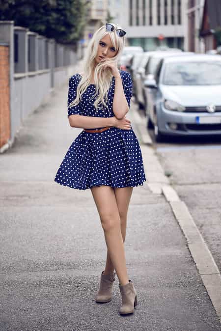 A woman wearing a blue polka dot skater dress and ankle booties