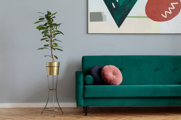 A green couch with abstract wall art above it and a gold potted plant next to it.