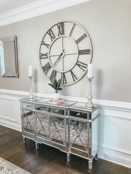 A mirrored buffet with a large open faced farmhouse clock above it.