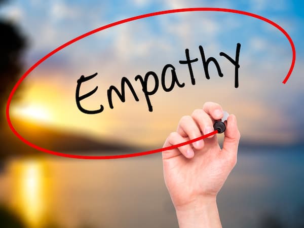 A person writing the word "empathy" in black marker on a visual board.