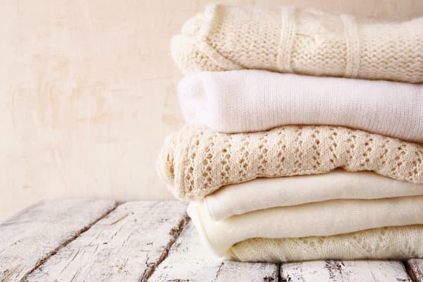 A stack of women's knit sweaters in neutral colors.