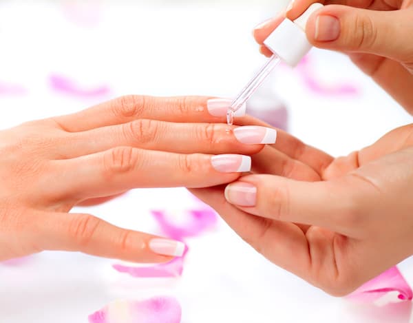 A woman having cuticle oil applied to her nails during a manicure.