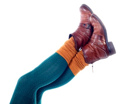 A woman wearing blue jeggings, yellow socks, and brown shoes holding up her legs.