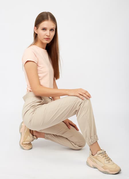 A woman in a light pink shirt and khaki pants with khaki sneakers.