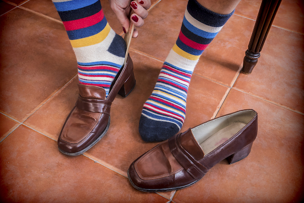A woman putting on a colorful pair of striped socks with a pair of brown shoes.