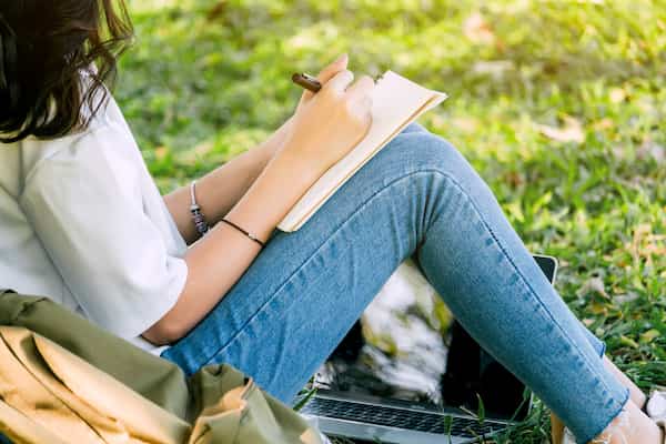 A woman sitting in the grass writing in her journal.