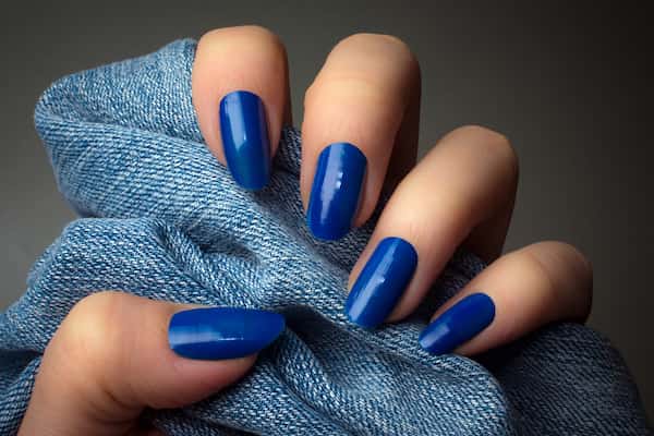 A woman's hand with bright blue nails holding onto blue denim jeans.