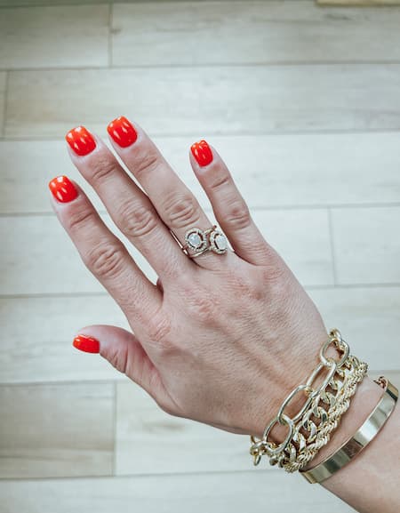 A woman's hand with red nails, gold rings, and gold bracelets.
