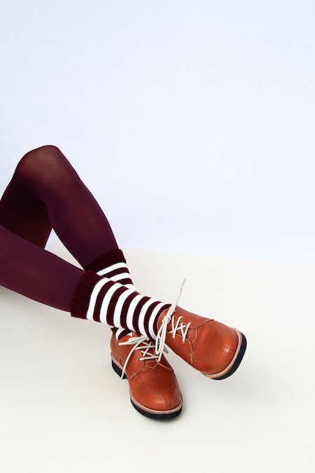A woman wearing maroon leggings, striped socks, and brown shoes.