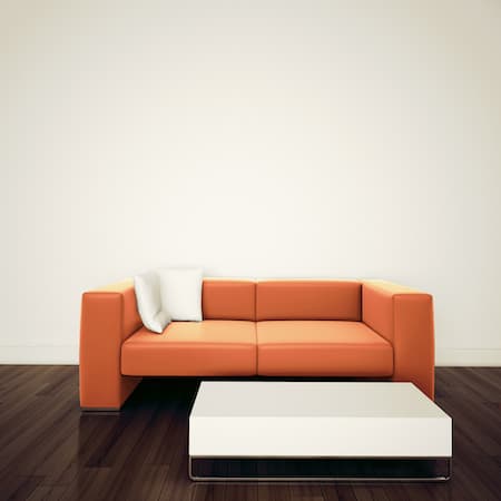 An orange contemporary couch with a white coffee table in front of it.