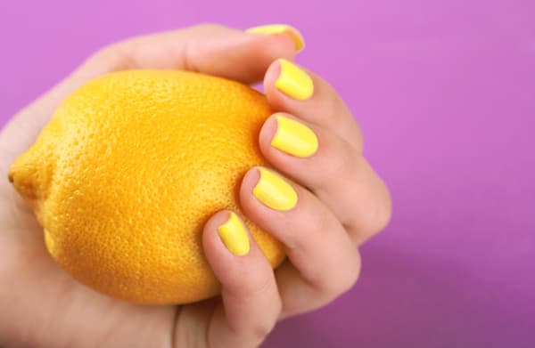 a woman with yellow nails holding a lemon.