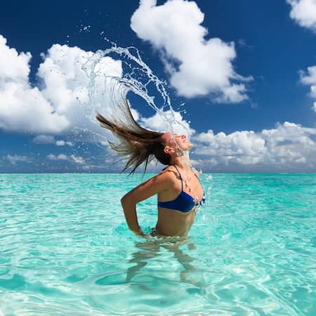 A woman in the ocean flipping her hair back.
