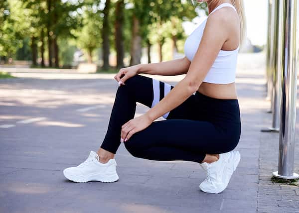 A woman wearing black leggings, a whit tank top, and white sneakers with no show socks.