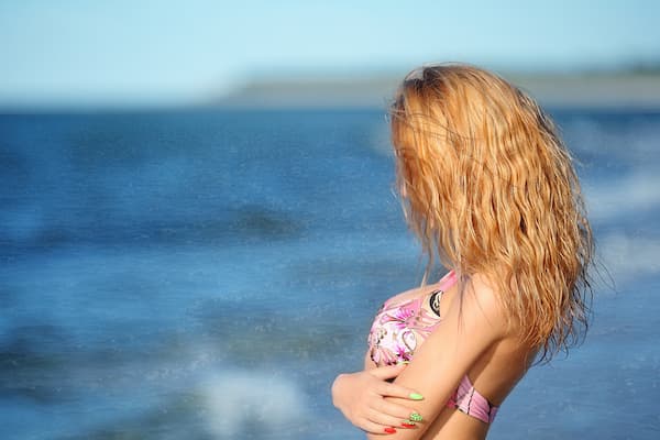 A woman with wavy hair standing in front of the ocean.