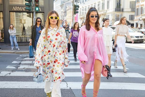 Two women walking across the street in pretty pastel colors. 