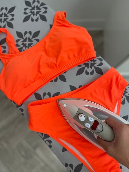 A woman ironing an orange bikini.