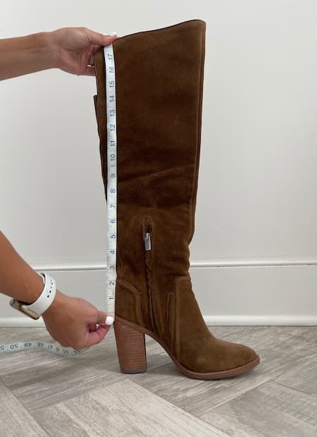 A woman measuring the shaft of a boot.