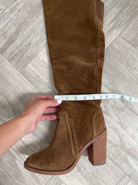 A woman measuring the ankle circumference of a brown boot.