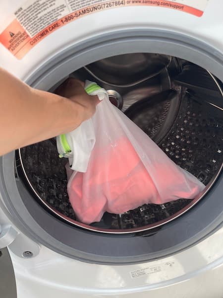 A woman putting an orange bathing suit into the washing machine.