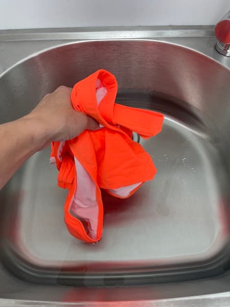 A woman putting an orange bikini into a sink full of water. 