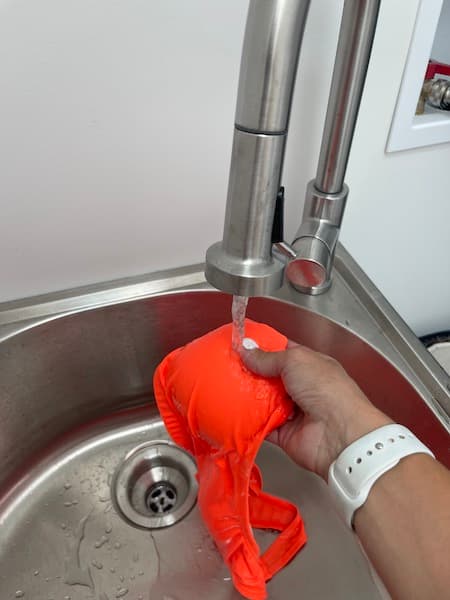 A woman soaking an orange bathing suit under water from a faucet. 