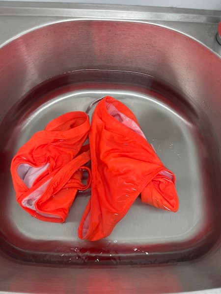 An orange bathing suit sitting in a sink full of water.