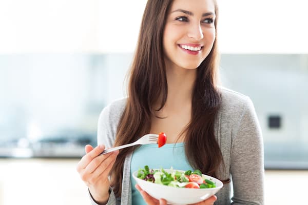 A smiling woman eating a salad.