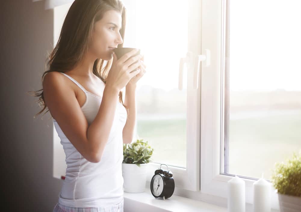 A woman having a cup of coffee and looking out the window.