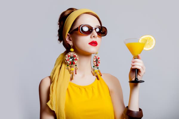 A woman wearing 70s earrings and clothes holding a drink.