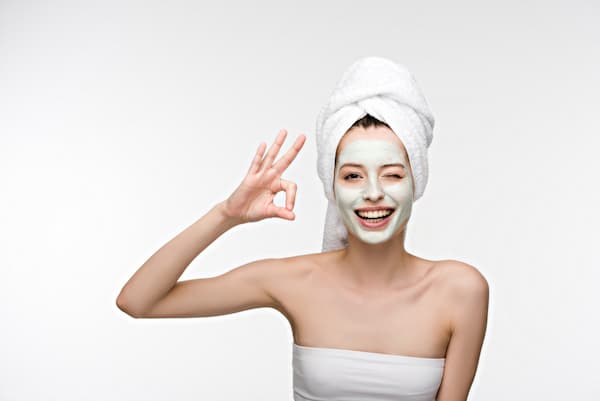 A woman with a fask mask on and a towel on her hair.