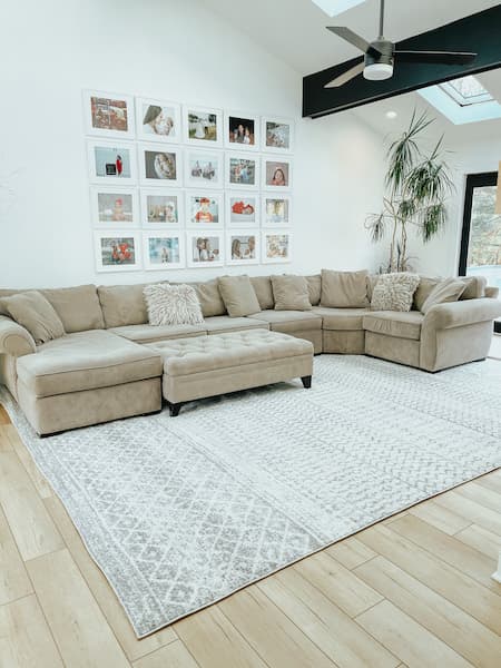 A grey polypropylene rug under a grey sofa in a living room.