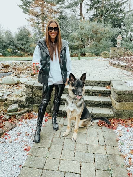 A smiling woman in patent faux leather pants standing with her german shepherd dog.