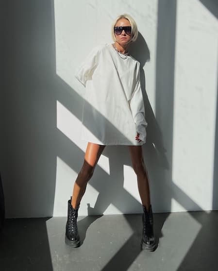 A woman wearing a long sleeve white t-shirt dress and black combat boots.