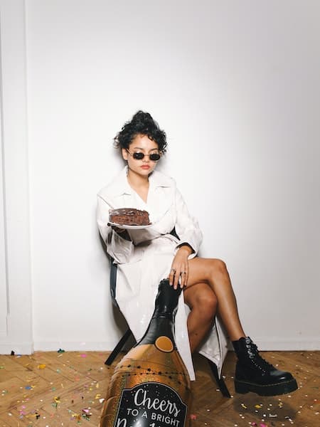 A woman sitting down wearing a white trench coat and black combat boots.