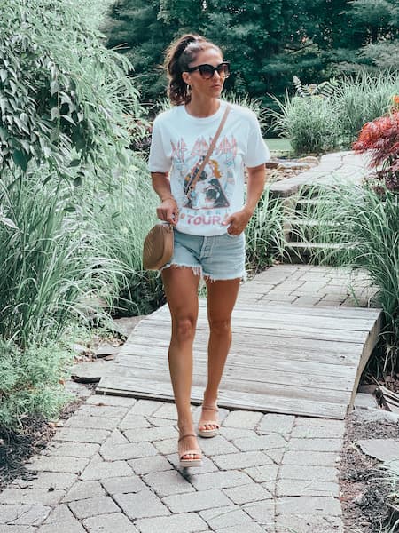 A woman wearing a graphic tee, denim cutoff shorts, and wedges.