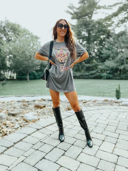 A woman wearing a graphic t-shirt as a dress with knee high boots.