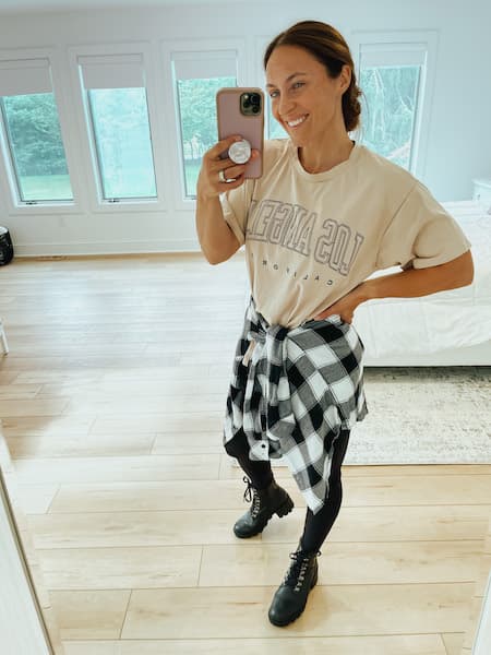 A woman wearing a graphic tee with leggings, combat boots, and a flannel around her waist.