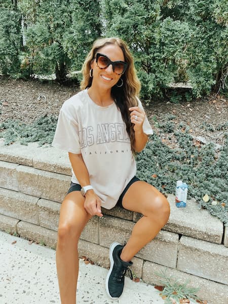 A woman wearing a graphic tee, black bike shorts, and black sneakers.
