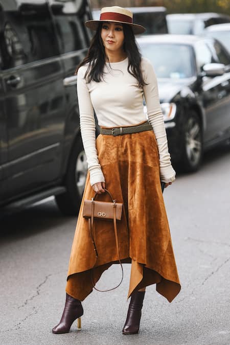 A woman wearing a long sleeve top, midi skirt, and ankle boots.