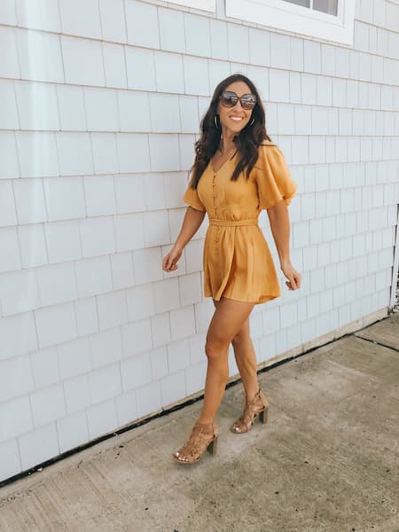A woman wearing a yellow romper walking past a builing.