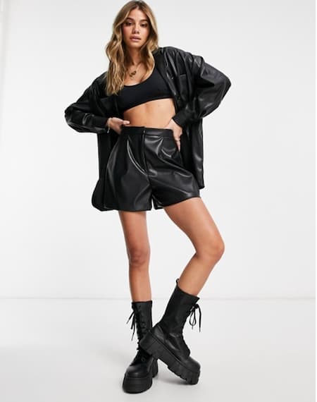 A woman wearing leather shorts, a bralette, a blazer, and combat boots.