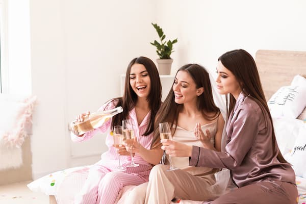 Women pouring champagne at a bachelorette slumber party.