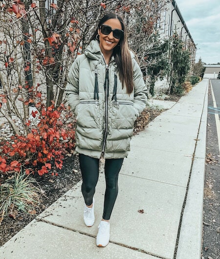 woman wearing a green winter coat, white sneakers, and black leggings