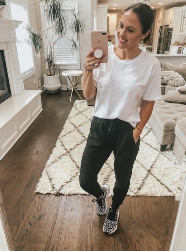 A woman taking a mirror selfie wearing black joggers, a white tshirt, and leopard print sneakers