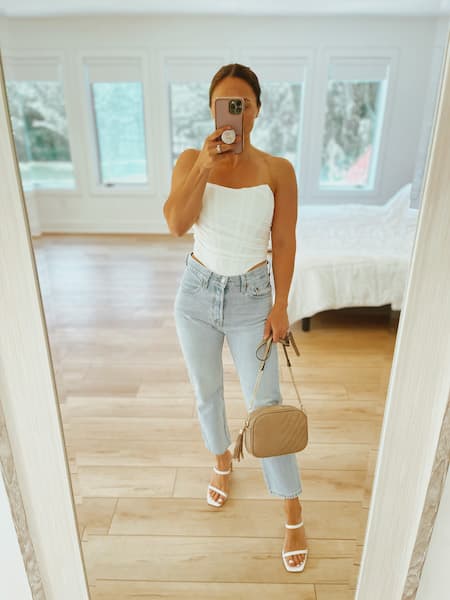 A woman taking a selfie in a white bustier top and mom jeans