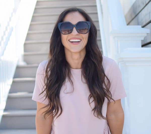 A smiling woman wearing a pink shirt and black sunglasses.