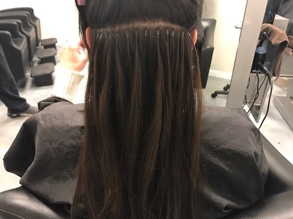 The back of a womans hair who is having microbead hair extensions installed.